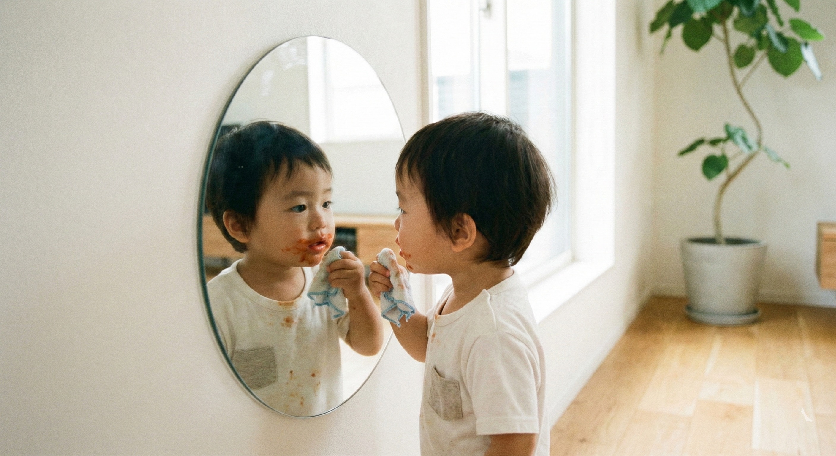 低い位置に貼られたアクリルミラーで顔を見る子ども